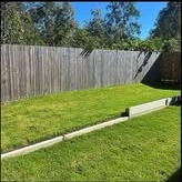 Mowed backyard against a grey wood fence and a stone edge