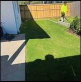 Worker in a neon shirt blowing a mowed backyard