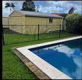 Mowed lawn beside a pool, metal fence, and a small shed