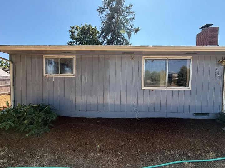 House siding mid pressure washing: left still oxidized, right cleaned, mulch bed in front